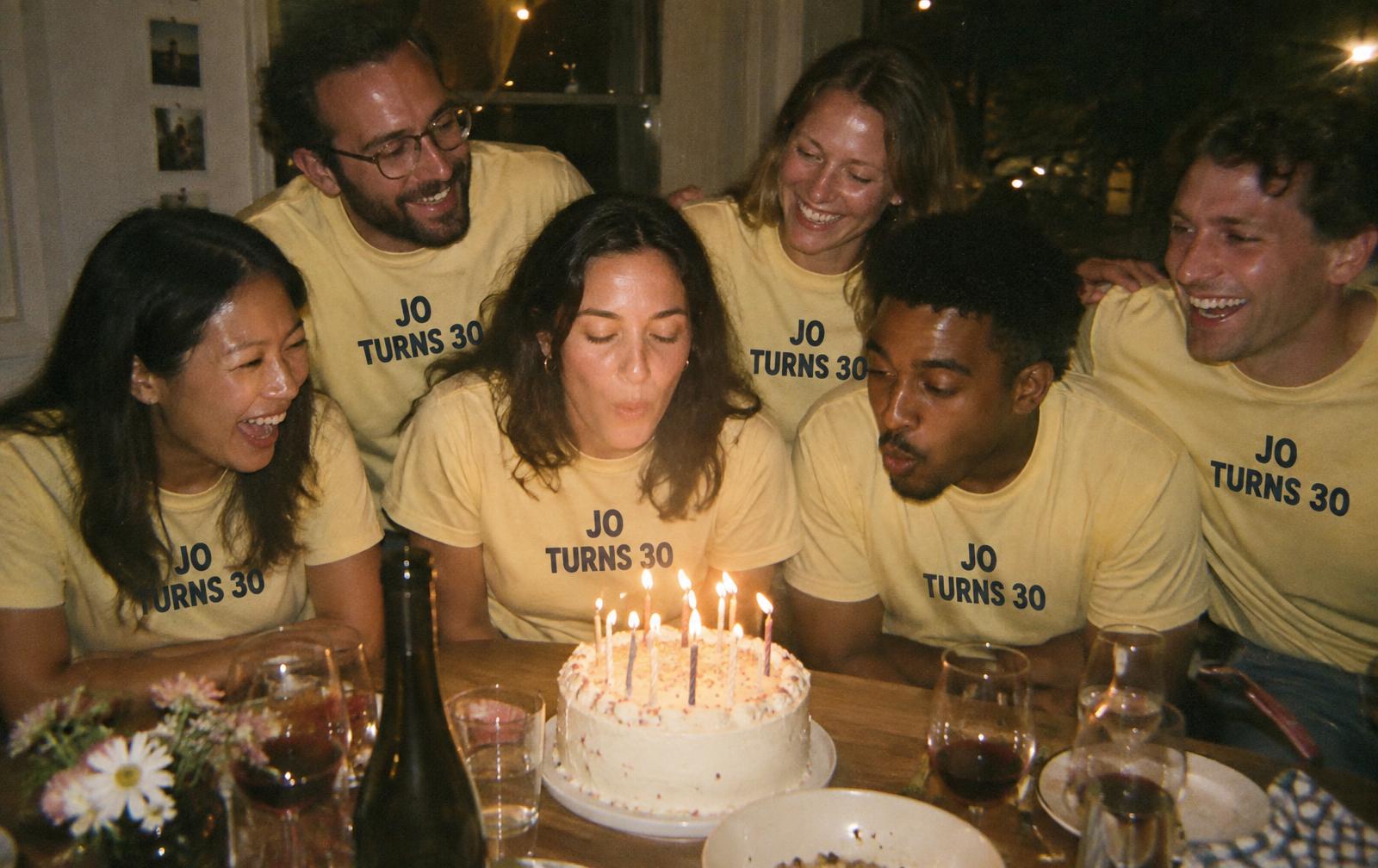 Friends in matching butter yellow Jo Turns 30 tees blowing out birthday candles