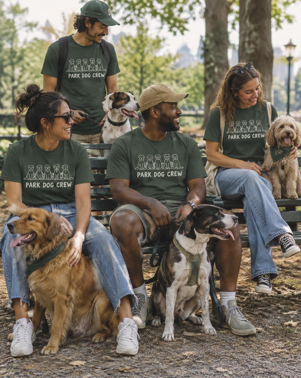 Friends in green Park Dog Crew tees sit on a park bench with their dogs, laughing together.