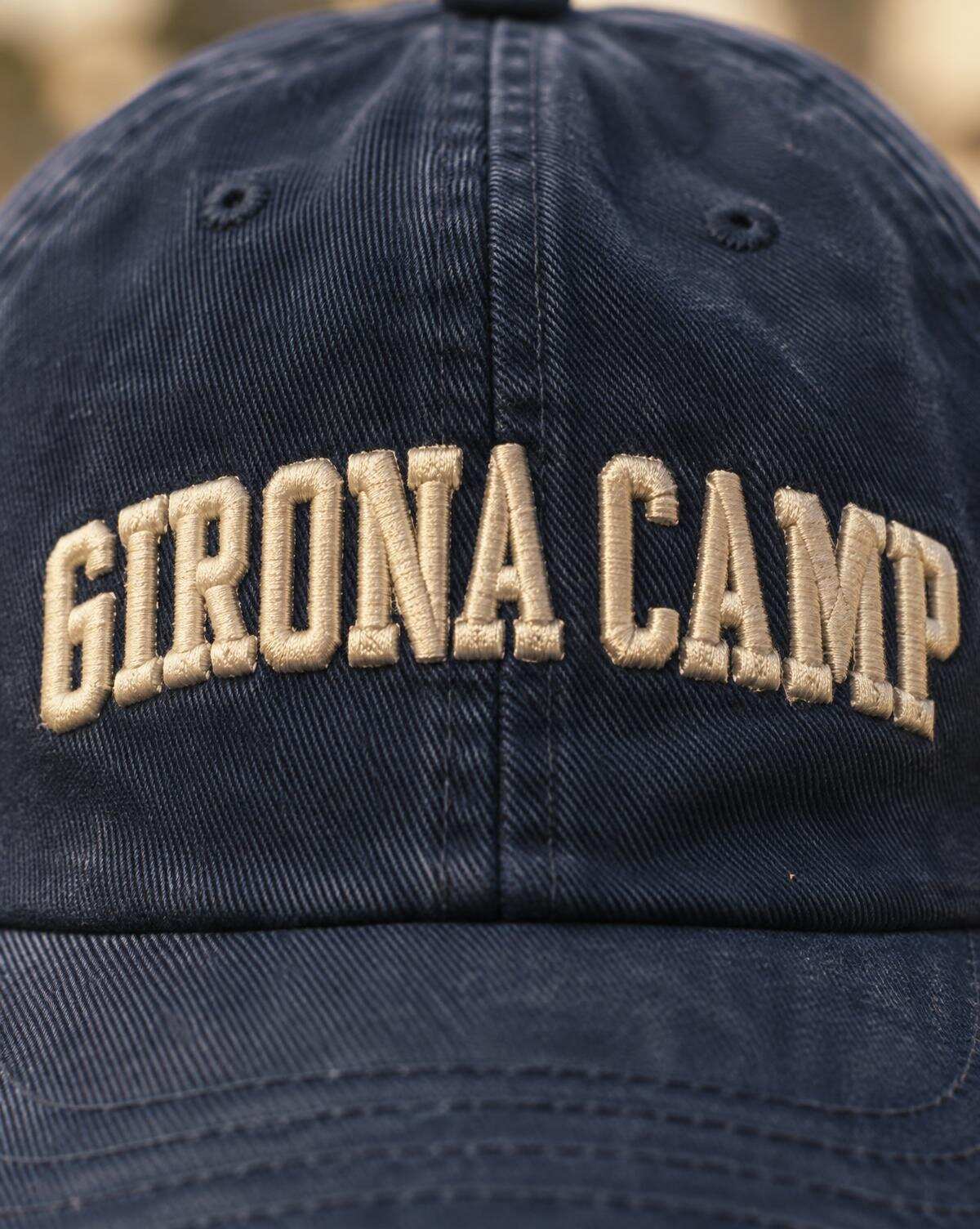 Macro of raised cream embroidered Girona Camp lettering on a navy cap