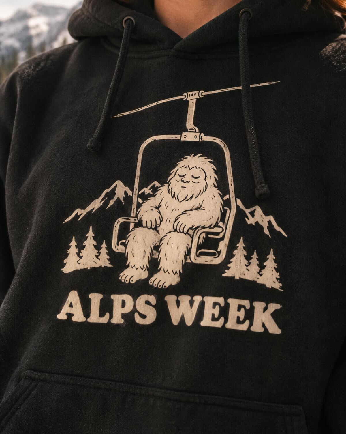 Close-up of a cream sleepy yeti on a chairlift and Alps Week lettering on a black hoodie