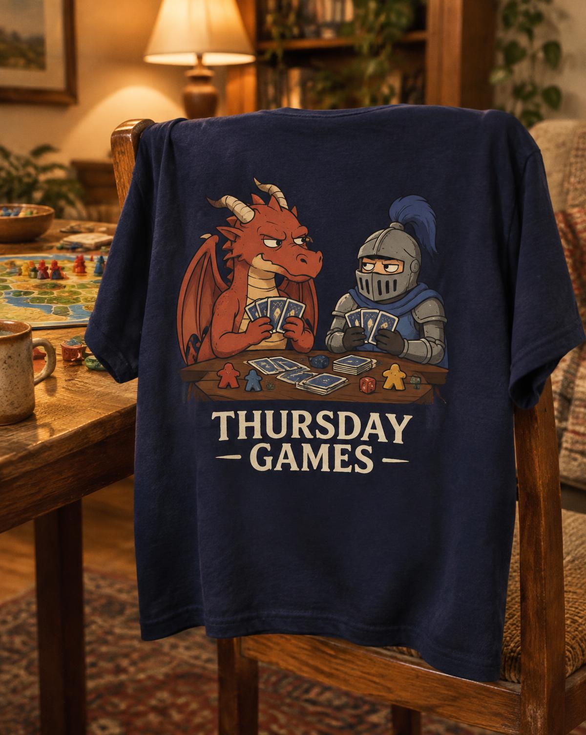 Navy Thursday Games tee with a grumpy red dragon and knight playing cards, draped over a chair by a game table.