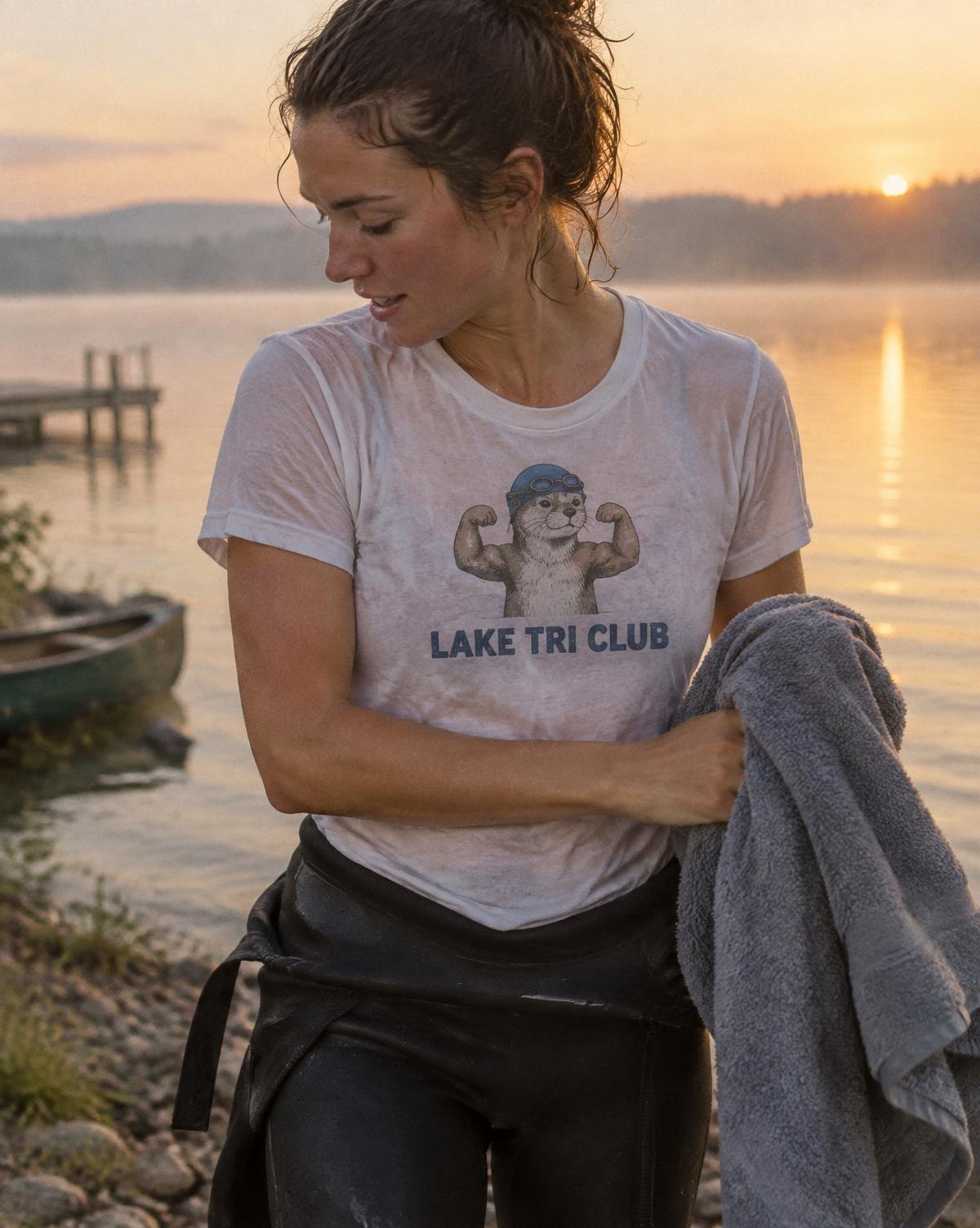 Swimmer in a white Lake Tri Club tee with a flexing otter in goggles, towel in hand by a misty lake.
