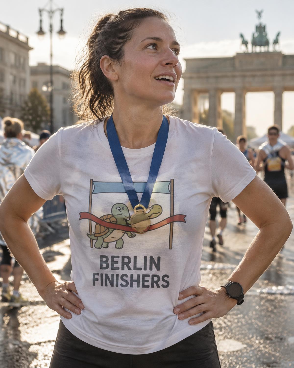 Proud runner in a white Berlin Finishers tee with a tortoise breaking the tape, medal on, near the gate.