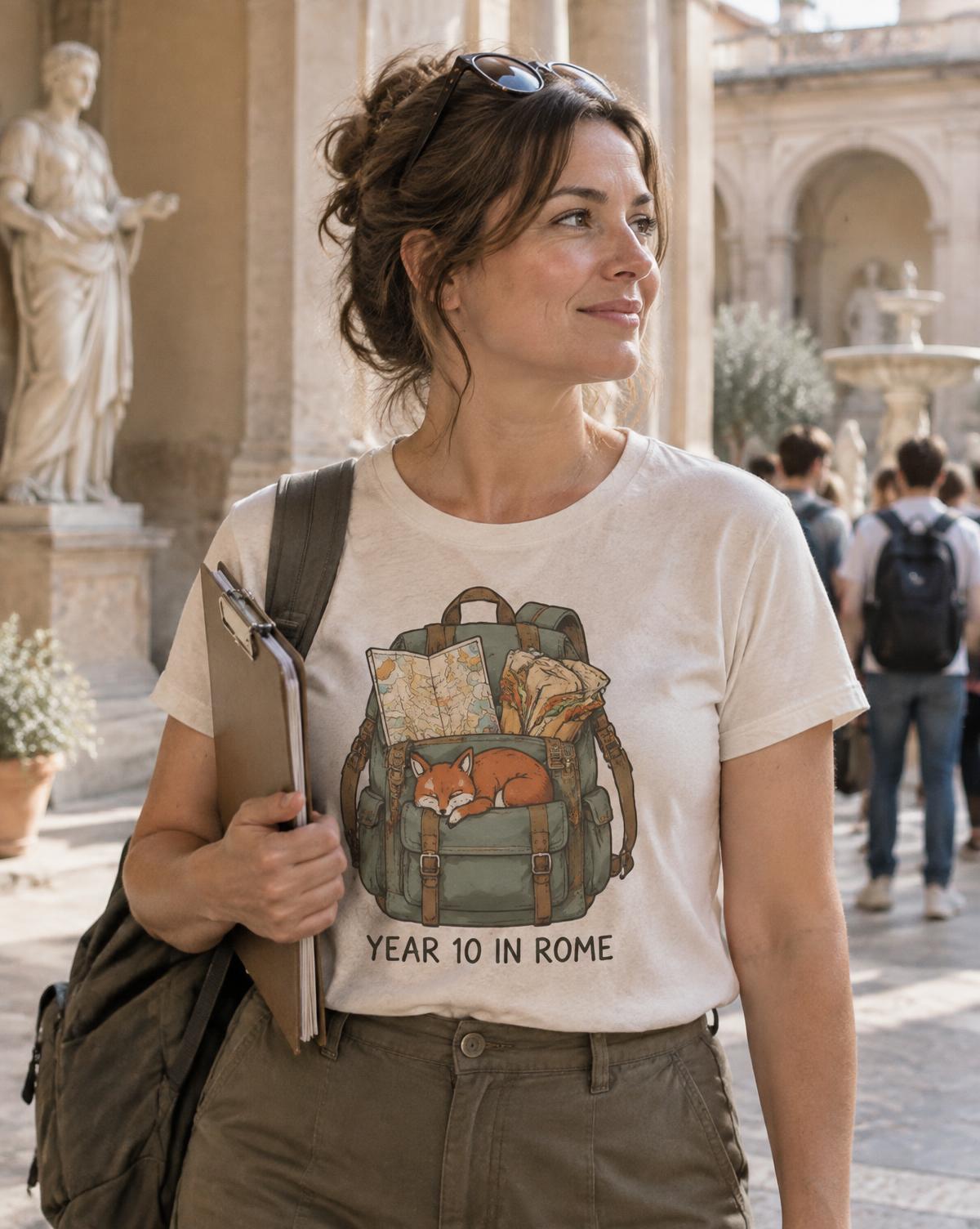 Teacher in a cream Year 10 In Rome tee with a fox asleep in a backpack, holding a clipboard in a square.