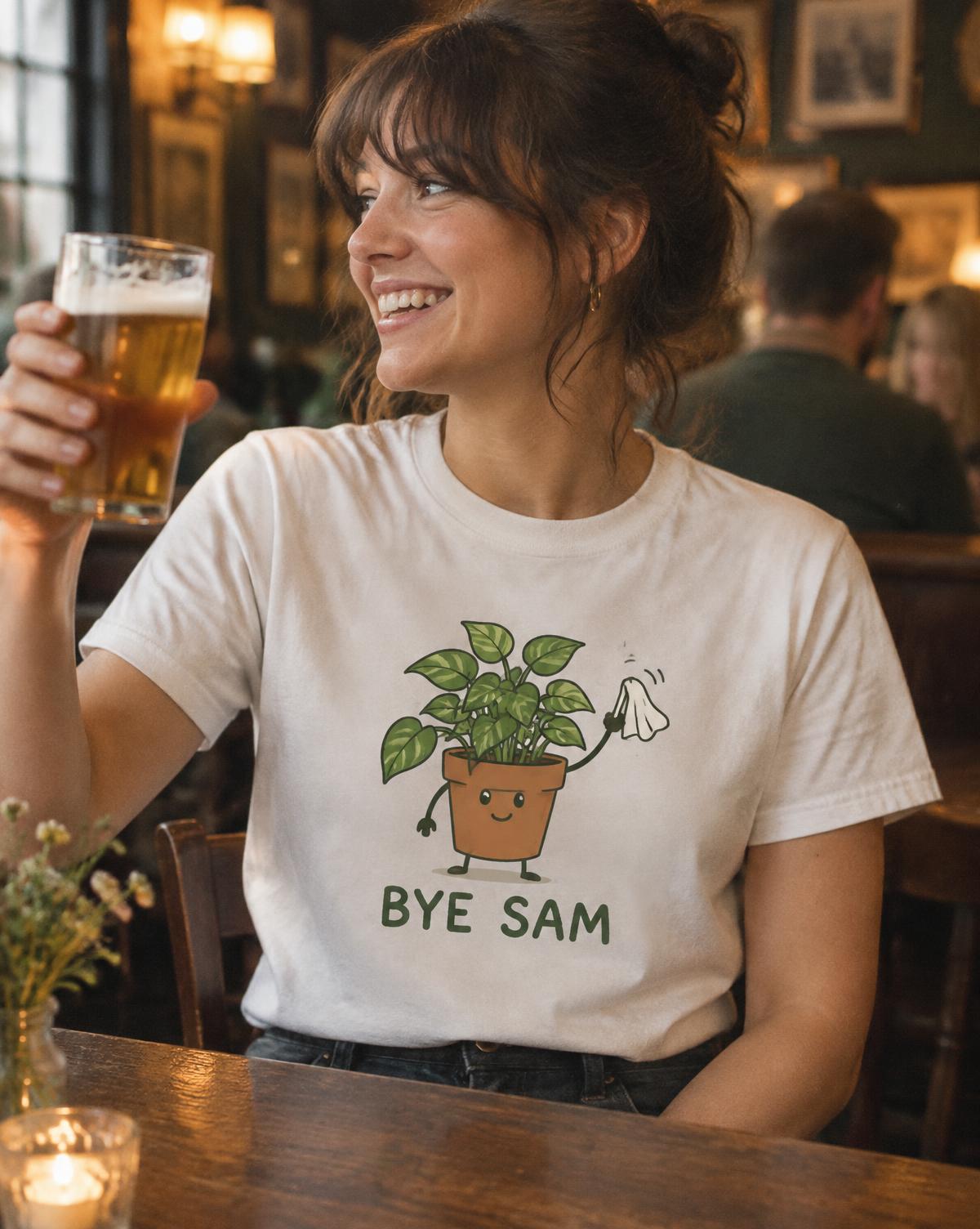 Woman in a white Bye Sam tee with a waving potted plant raising a pint in a warm pub.