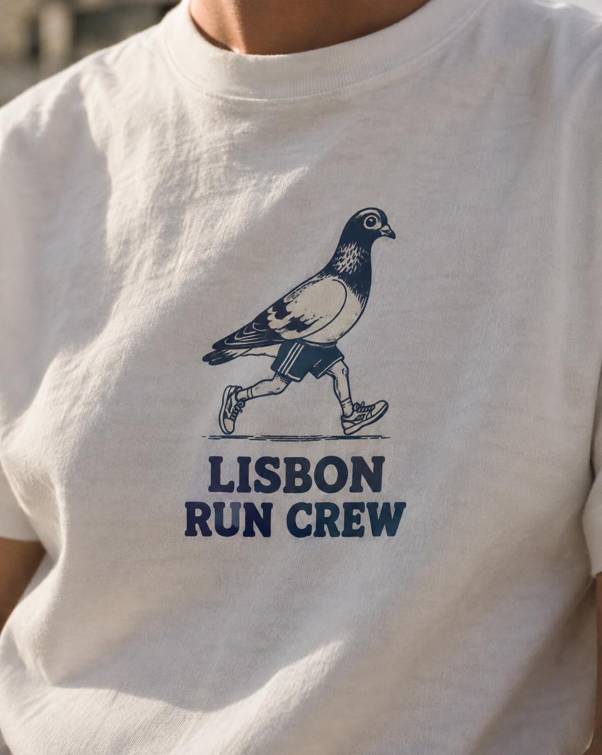 Close-up of a navy printed pigeon in running shorts and Lisbon Run Crew lettering on a white tee