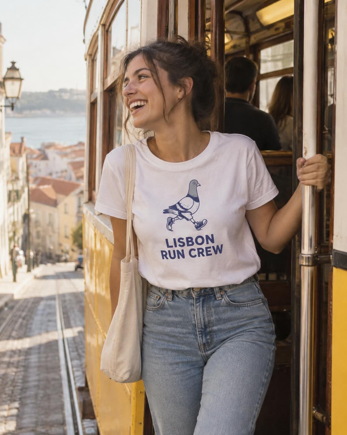 Woman laughing on a Lisbon tram step in a white tee with a navy Lisbon Run Crew pigeon print